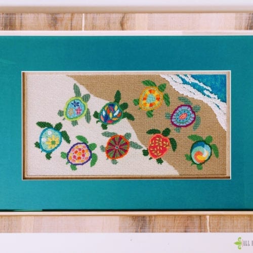 detail of framed turtle needle point with turquoise mat and heavy wood grain frame.